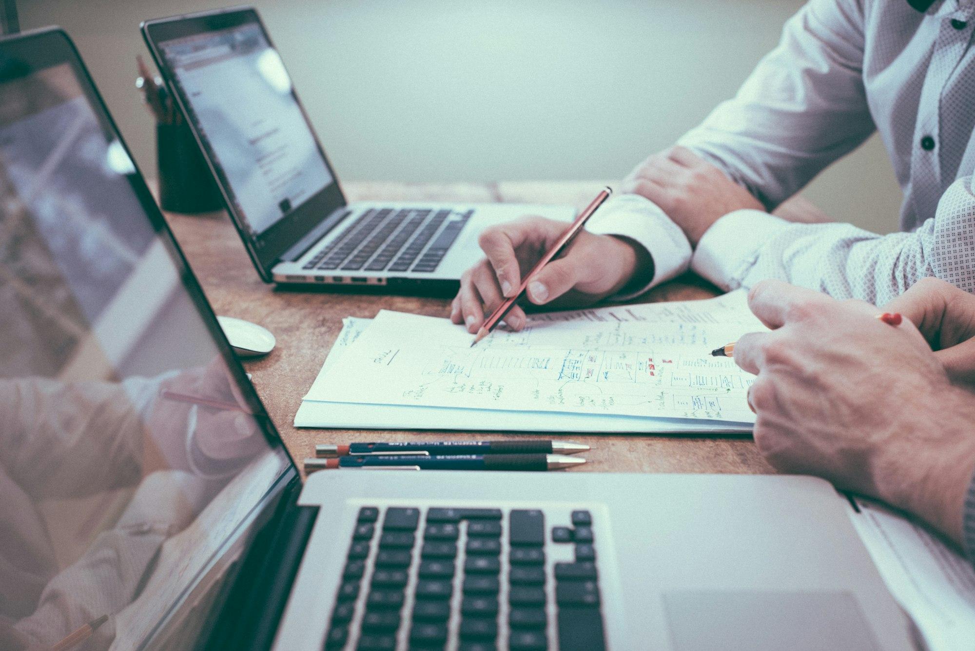Hands writing financial notes beside laptops at a Vaughan accounting firm