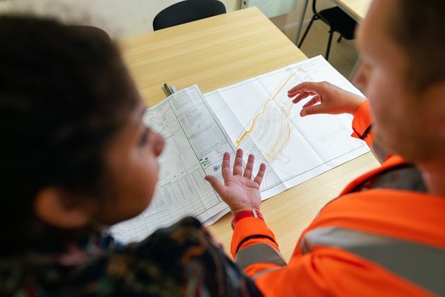 Engineer in a safety vest reviewing a civil site plan with a colleague at a desk in Hamilton